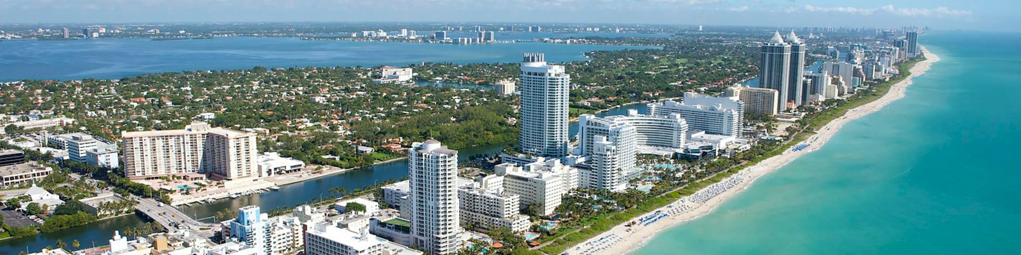Aerial view of a tropical beachfront city with high-rise hotels, sandy coast, and calm blue ocean stretching into the distance.