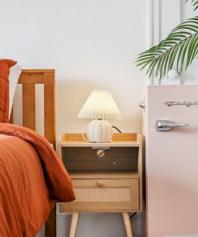 A modern bedroom corner with orange bed linens, a bedside cabinet, lamp, and a potted palm bringing fresh greenery indoors.