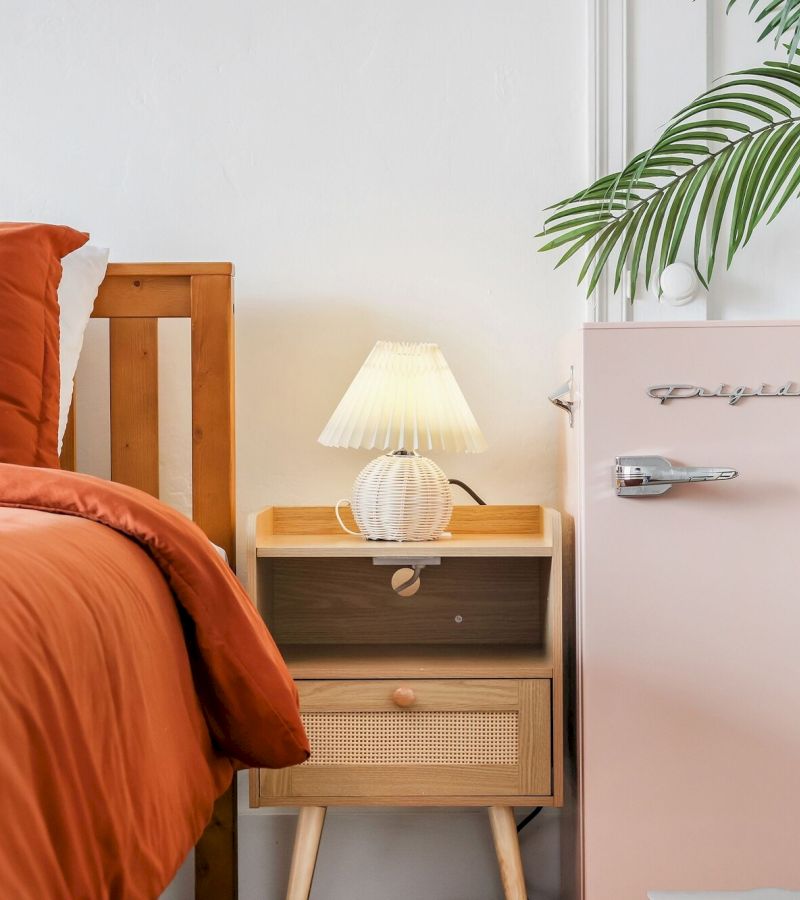 A cozy guest room with orange bedding, a wooden nightstand, and a small pink fridge.