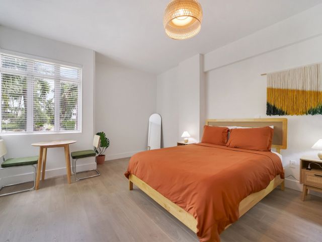 A wide view of a guest room with a large bed, window, and furniture.