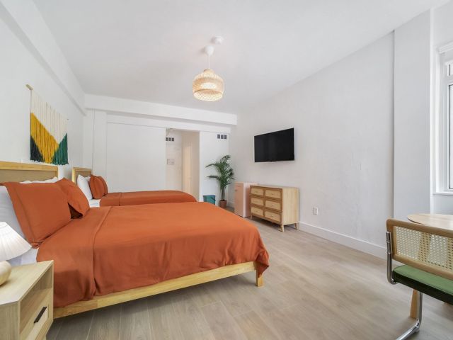 A wide view of a hotel room with two beds, a TV, and a window.