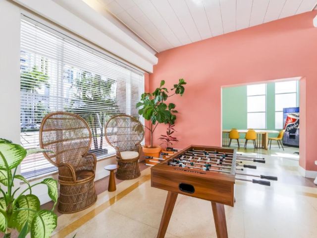 A brightly lit game room with a foosball table, wicker chairs, and plants.