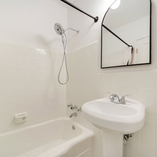 A modern bathroom with a bathtub, showerhead, pedestal sink, and a large mirror overhead.