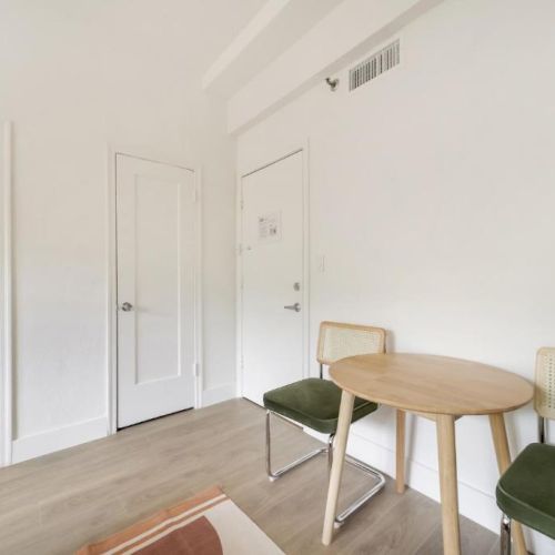 Bright room with a round wooden table, green chairs, two white doors, and some plants by the corner.