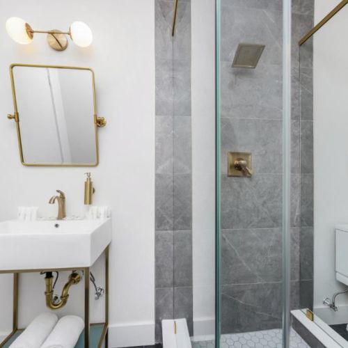 Modern bathroom with gold fixtures: white vanity and mirror, glass shower, and a toilet.