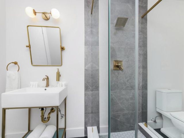 A modern bathroom with a white sink, gold fixtures, and a glass-enclosed shower.