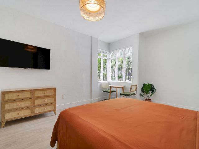 A wide view of a guest room with a bed, dresser, TV, table, and chairs.