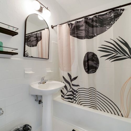 A bright bathroom with a bathtub and decorative shower curtain, plus a small sink and towel rails.
