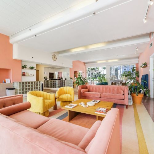 Bright modern lounge with colorful sofas, a wooden coffee table, potted plants, and a reception counter in a pastel interior.