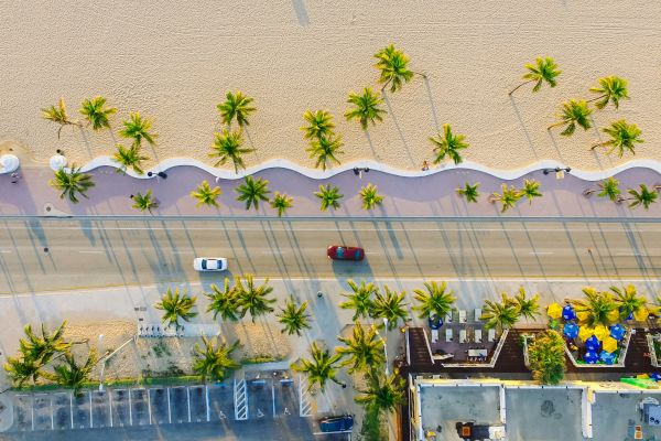 Aerial view of a poolside courtyard with palm trees, cars, and sun loungers along a wavy wall.