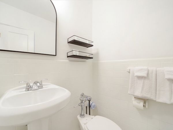 Bright hotel bathroom with a white sink, toilet, chrome faucet, and stacked glass shelves with towels.