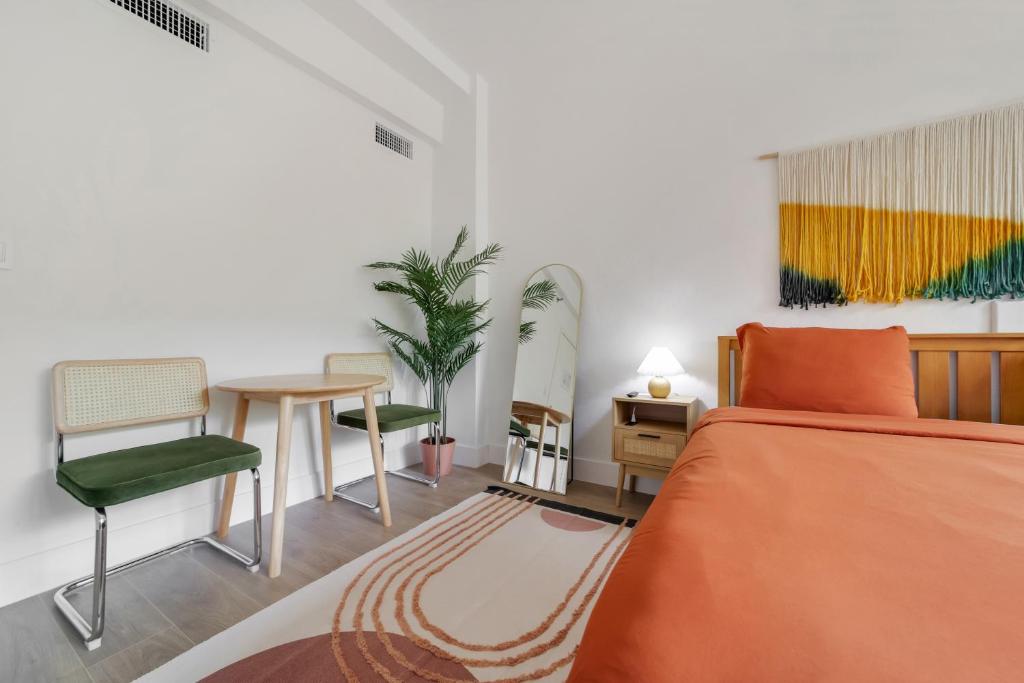 A wide view of a guest room with a bed, two chairs, a small table, and a potted plant.