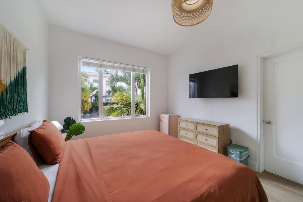 A wide view of a guest room with a double bed, dresser, TV, and window