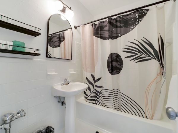A small bathroom with white tiles, a pedestal sink, a tub, and a zebra-themed shower curtain under bright ceiling lights.