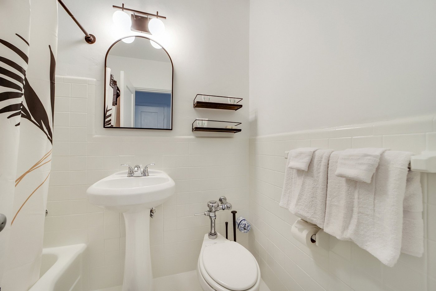 A clean bathroom with white tiles, a pedestal sink, toilet, and towels.