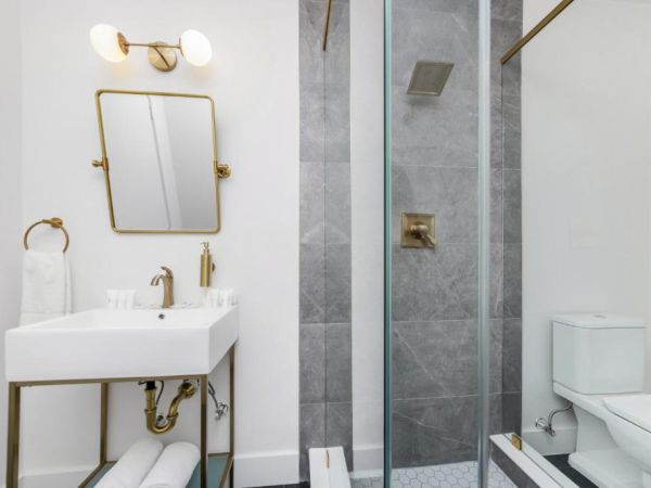 A modern bathroom with a white vanity, gold-framed mirror, and a glass shower plus white toilet.