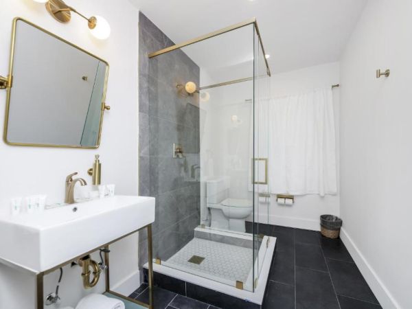 A modern bathroom with a white sink, brass fixtures, dark tile floors, and a glass shower with a white curtain.