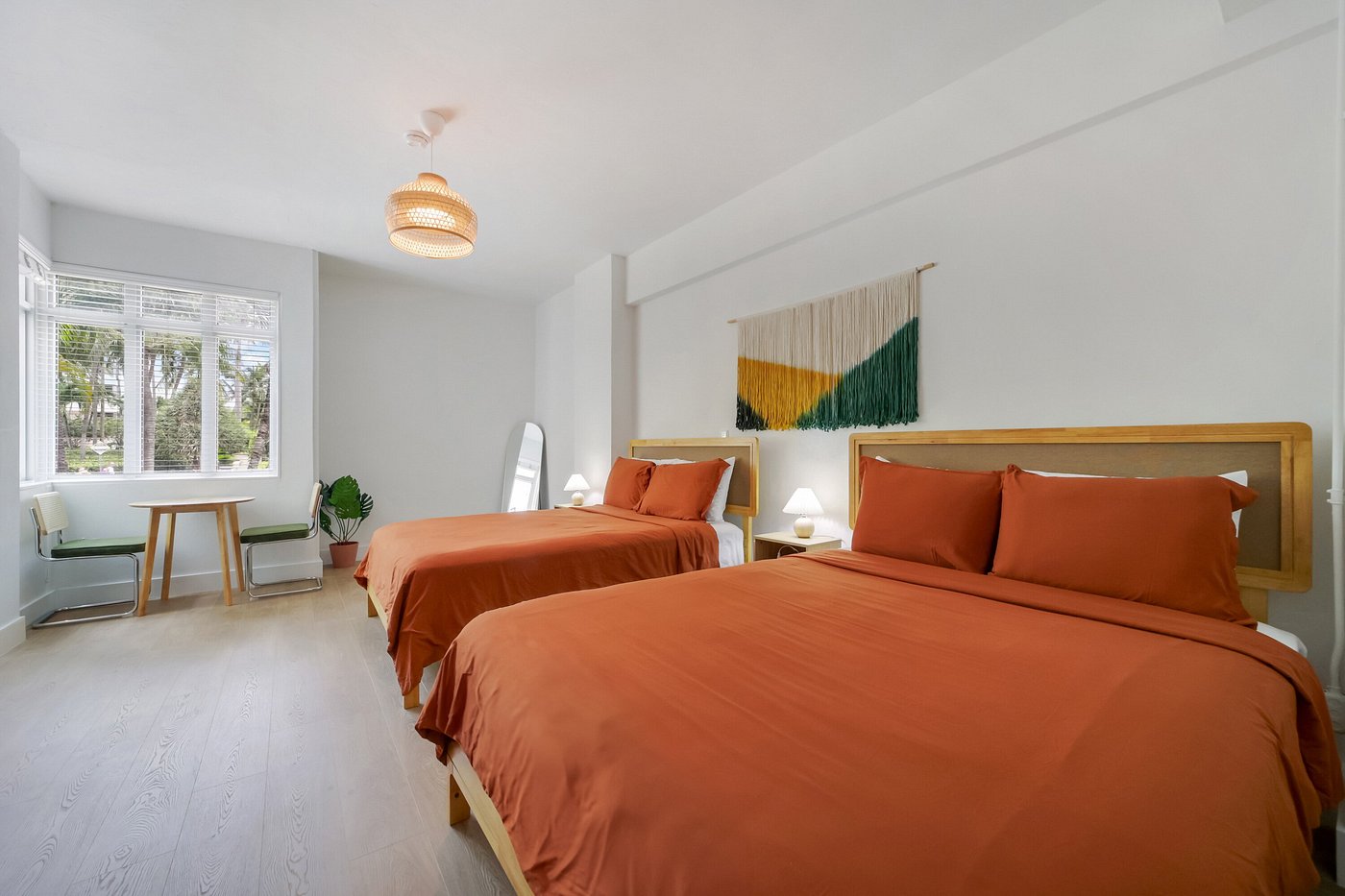 A bright and airy hotel room with two twin beds, a window, and a small table with chairs.