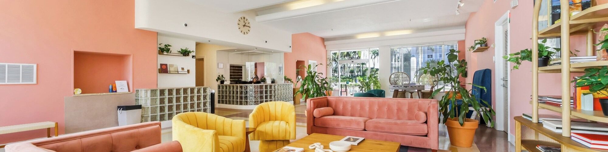 Bright lobby lounge with colorful sofas, a wooden coffee table, potted plants, and glass-and-mirror wall accents.