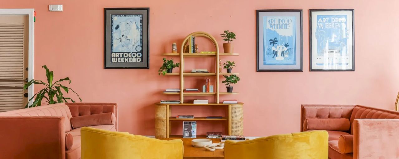 A lounge area with pink walls, yellow chairs, and a bookshelf with posters.