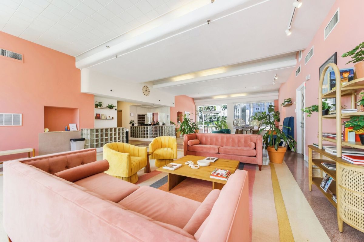 A brightly lit lobby with pink couches, yellow chairs, and a wooden coffee table.